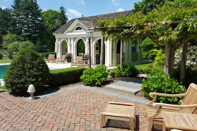 Modelo de casa de la piscina y piscina alargada clásica grande rectangular en patio trasero con adoquines de ladrillo