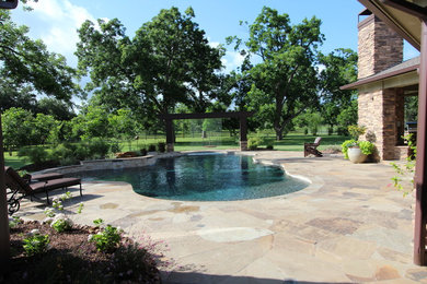 Diseño de piscina con fuente rústica grande a medida en patio trasero con suelo de baldosas
