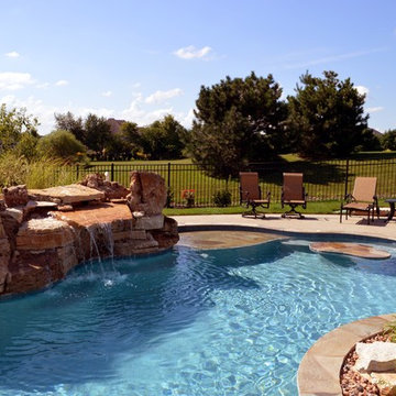 Free form pool with stone table, sun shelf, water feature, and outdoor kitchen,