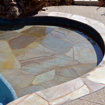 Free form pool with stone table, sun shelf, water feature, and outdoor kitchen,