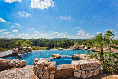 Example of a huge classic backyard custom-shaped and stone infinity pool fountain design in Austin