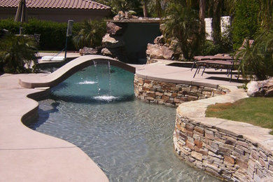 Ejemplo de piscina con fuente alargada exótica grande a medida en patio trasero con losas de hormigón