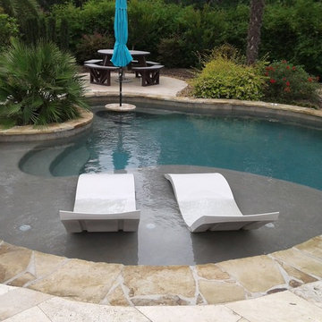 Freeform pool with tanning ledge, ledge loungers, rock waterfall, cocktail table