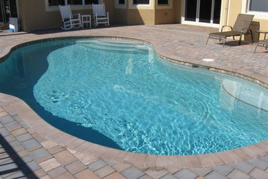 Example of a mid-sized island style backyard brick and custom-shaped natural pool design in Miami