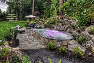 Diseño de piscina con fuente elevada tradicional renovada pequeña tipo riñón en patio trasero con adoquines de piedra natural