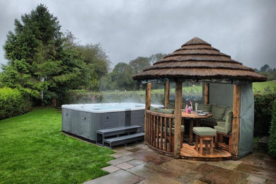 This is an example of a medium sized rural back hot tub in Sussex with natural stone paving.