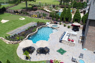 Diseño de piscina natural rústica grande a medida en patio trasero con adoquines de hormigón