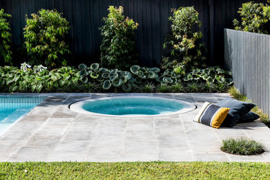 Medium sized modern back custom shaped swimming pool in Melbourne with with pool landscaping and natural stone paving.