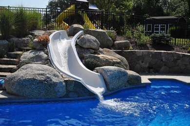 Ejemplo de piscina con fuente grande a medida en patio trasero con adoquines de piedra natural