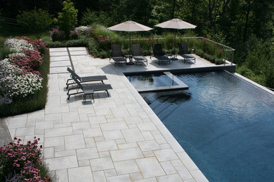 Modelo de piscina infinita contemporánea grande rectangular en patio trasero con adoquines de hormigón