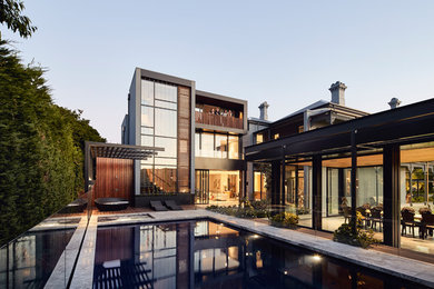 Modelo de casa de la piscina y piscina elevada actual grande rectangular en patio trasero con adoquines de piedra natural