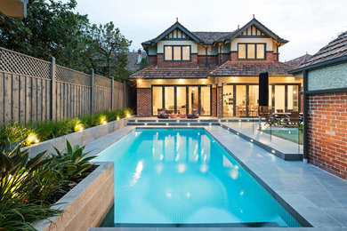Design ideas for a medium sized traditional back custom shaped lengths swimming pool in Melbourne with a water feature and natural stone paving.