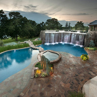 Photo of an expansive eclectic backyard custom-shaped natural pool in Oklahoma City with a water feature and natural stone pavers.