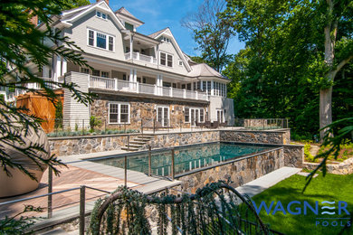 Example of a large classic backyard stone and rectangular infinity pool fountain design in New York