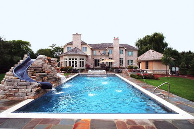 На фото: большой спортивный, прямоугольный бассейн на заднем дворе в классическом стиле с водной горкой и покрытием из каменной брусчатки с