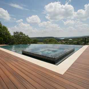 Esempio di una grande piscina a sfioro infinito design rettangolare dietro casa con una vasca idromassaggio e pedane