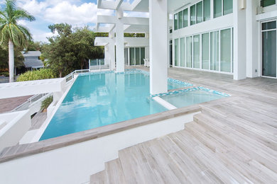 На фото: большой прямоугольный бассейн-инфинити на заднем дворе в стиле модернизм с джакузи и покрытием из плитки