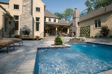 Foto de piscina con fuente alargada clásica grande a medida en patio trasero con adoquines de piedra natural