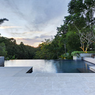 Design ideas for a large tropical backyard rectangular infinity pool in Sunshine Coast with natural stone pavers.
