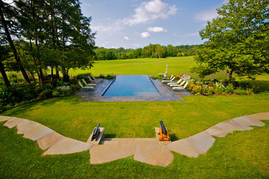 Example of a large classic backyard stone and rectangular infinity pool fountain design in Wilmington