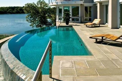 This is an example of a medium sized contemporary back custom shaped infinity swimming pool in Boston with a water feature and concrete paving.