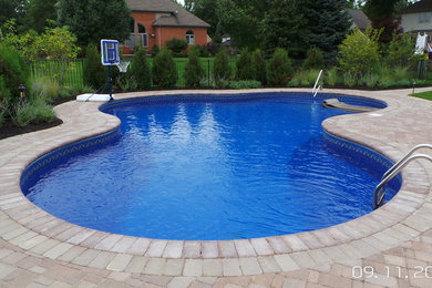 Medium sized modern back custom shaped swimming pool in Detroit with brick paving.