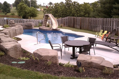 Modelo de piscina con tobogán natural rústica grande a medida en patio trasero con suelo de hormigón estampado