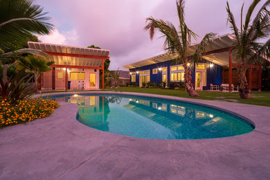 Example of an island style backyard concrete paver and custom-shaped pool house design in Hawaii