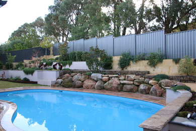 Imagen de piscina actual de tamaño medio a medida en patio trasero con adoquines de piedra natural