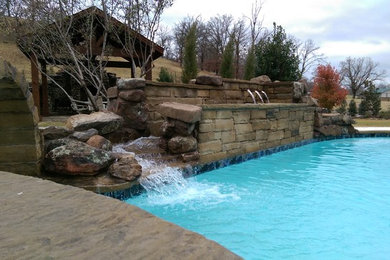 Imagen de piscina con fuente alargada rústica tipo riñón en patio trasero con adoquines de piedra natural