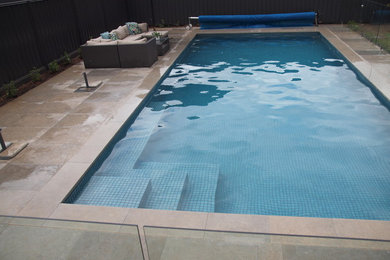 Ejemplo de piscina alargada actual grande rectangular en patio trasero con adoquines de piedra natural