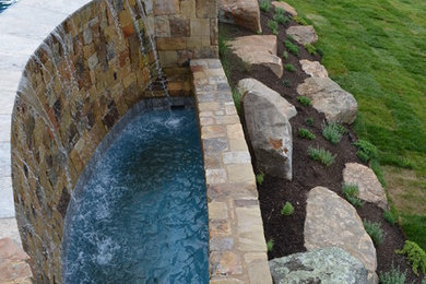 Ejemplo de piscina con fuente infinita tradicional extra grande a medida en patio trasero con adoquines de piedra natural