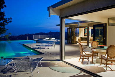 Large contemporary back l-shaped infinity swimming pool in Orange County with concrete paving.