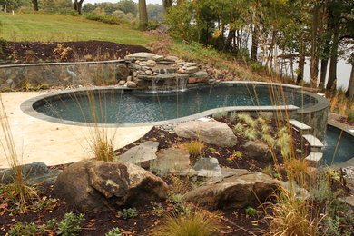 Cette image montre une piscine arrière et à débordement traditionnelle de taille moyenne et sur mesure avec des pavés en pierre naturelle et un point d'eau.
