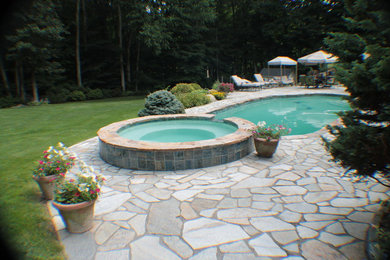 Immagine di una grande piscina moderna personalizzata dietro casa con una vasca idromassaggio e pavimentazioni in pietra naturale