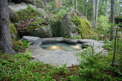 Example of a large mountain style backyard stone and custom-shaped natural hot tub design in Other