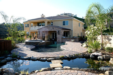 Inspiration for a large mediterranean back custom shaped hot tub in Los Angeles with brick paving.