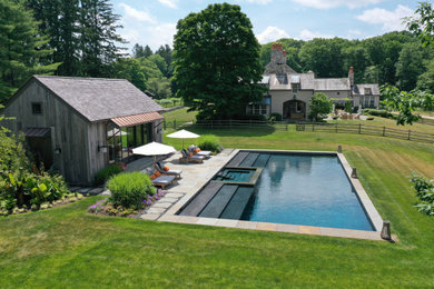 На фото: большой прямоугольный бассейн на заднем дворе в классическом стиле с домиком у бассейна и покрытием из каменной брусчатки