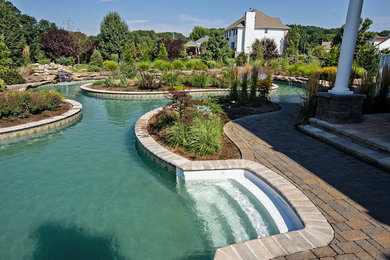 This is an example of a large contemporary back custom shaped natural swimming pool in New York with brick paving.