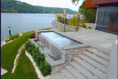 This is an example of a contemporary back custom shaped infinity hot tub in New York with natural stone paving.