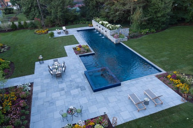 Ispirazione per un'ampia piscina monocorsia minimal rettangolare dietro casa con una vasca idromassaggio e pavimentazioni in pietra naturale
