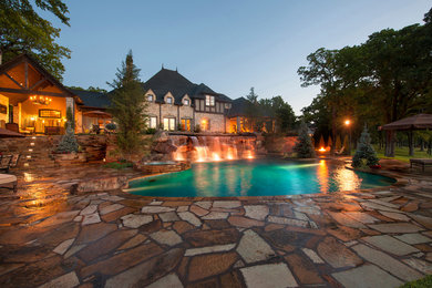 Immagine di una grande piscina naturale chic personalizzata con pavimentazioni in pietra naturale e una vasca idromassaggio