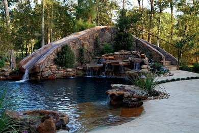 Idée de décoration pour une grande piscine naturelle et arrière chalet sur mesure avec un toboggan et du béton estampé.