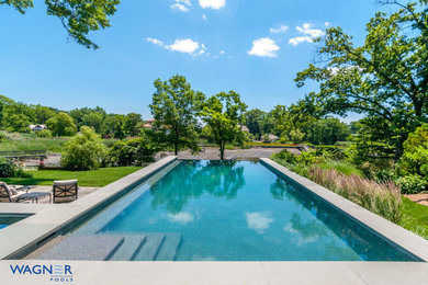 This is an example of a large traditional back rectangular infinity swimming pool in New York with a water feature and natural stone paving.