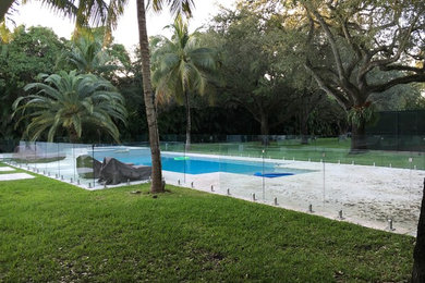 Large coastal back rectangular swimming pool in Miami with concrete slabs and fencing.