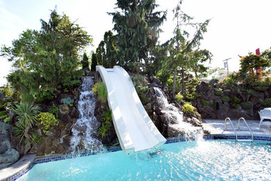Imagen de piscina con tobogán alargada contemporánea grande tipo riñón en patio trasero con adoquines de piedra natural