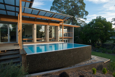 Cette photo montre une petite piscine à débordement et arrière moderne rectangle avec un point d'eau et une terrasse en bois.