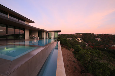 Diseño de piscina con fuente elevada minimalista grande rectangular en patio trasero con adoquines de hormigón
