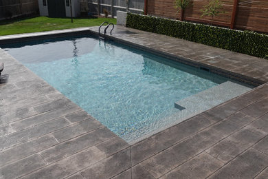 Modelo de piscina moderna de tamaño medio rectangular en patio trasero con suelo de hormigón estampado