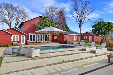 Ejemplo de piscina alargada de estilo de casa de campo grande rectangular en patio trasero con losas de hormigón